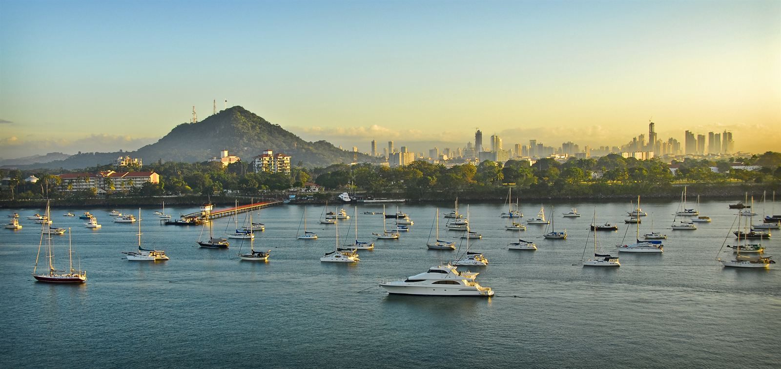 Sailboats at anchor in calm water with Ancon Hill and the Panama City skyline behind at sunset