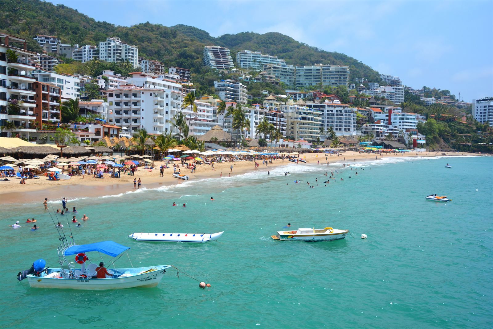 Swimmers and small boats off a sandy beach in Puerto Vallarta, with white hillside buildings behind